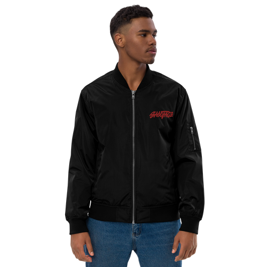 A man with short hair is wearing the UJ001 ▪ Bomber Jacket Iconic - Origem by C3 and blue jeans. The high-quality, recycled jacket features a red logo on the left chest area. He is standing with his arms relaxed at his sides, looking to his left against a plain white background.