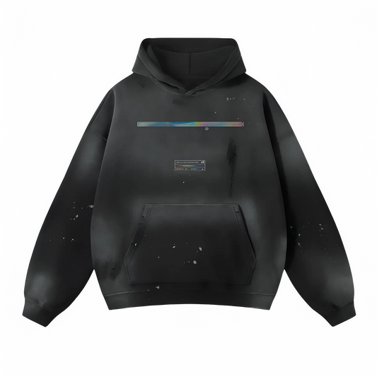 The ODMPOD Vintage Wash Frayed Fleece Hoodie (360 GSM) is a black hooded sweatshirt crafted from soft cotton. It features a colorful horizontal streak across the chest, a small rectangular graphic below it, and comes with a large front pocket. This casual piece showcases a distressed, paint-splattered design.