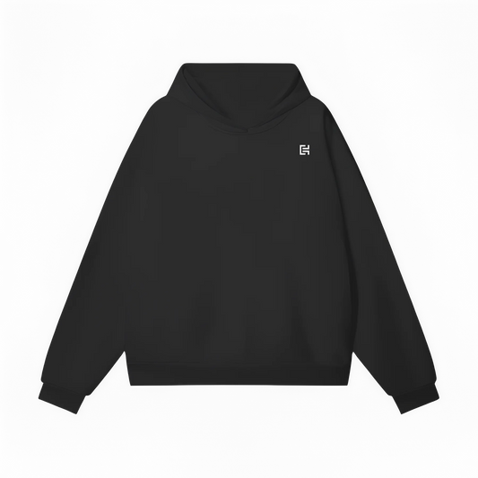 The UH020 Hoodie by ODMPOD is a black, unisex oversized hoodie with long sleeves and a front pocket. Made from thick cotton fabric, it showcases a small white geometric logo on the upper left chest area, reflecting a minimalist design. Ideal for winter wear, the hoodie maintains a plain black background.