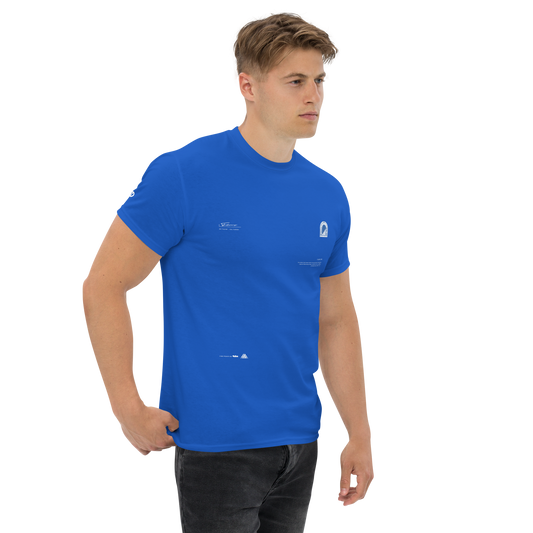 A young man with short, light brown hair is standing against a plain background. He is wearing a fitted blue UT045 ▪ T-Shirt by C3 and black jeans, perfect for streetwear outfits. The 100% cotton T-shirt has small white text and logos on the front and sleeves. He is looking to his left with a neutral expression.