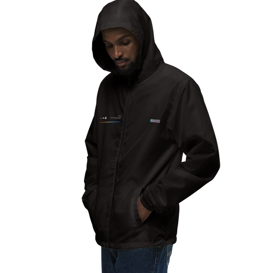 A man stands with his hands in his pockets, wearing a dark hoodie over an ultra-lightweight UW001 ▪ Windbreaker by C3. The background is entirely black, making his clothing and the small color accents on the jacket stand out. His hood is up, and he has a thoughtful expression.