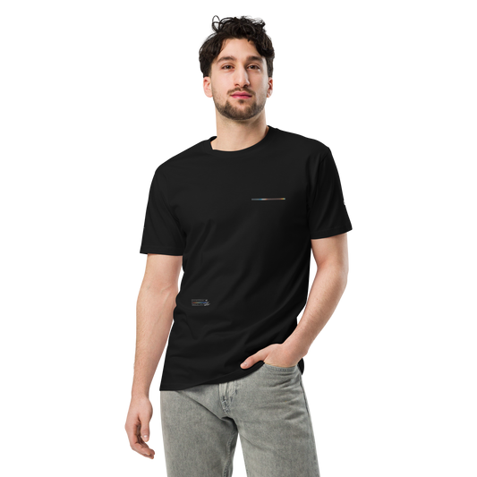 A man with short dark hair and a beard is standing against a plain background, wearing a C3 UT049 ▪ T-Shirt made from 100% combed cotton, featuring a small, subtle horizontal design near the left chest area. He has his left hand in the pocket of his light grey jeans and is looking ahead.