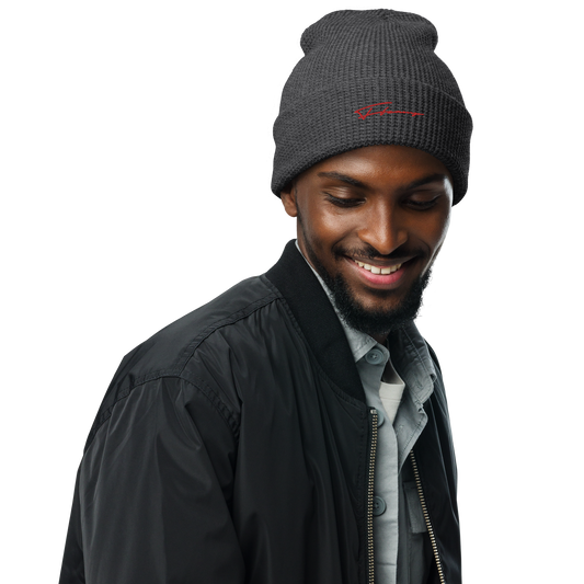 A man with a beard and mustache smiles while looking down. He is wearing a C3 UB001 ▪ Beanie in dark gray with an adjustable cuff, a black bomber jacket, and a light-colored shirt. The background of the image is transparent.