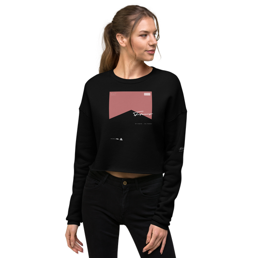 A woman with blonde hair tied back in a ponytail is wearing a trendy C3 WS002 ▪ Crop Sweatshirt with a pink geometric design and abstract graphics. She is looking to her left and has her right hand resting on her thigh. She is also wearing black jeans, blending fashion and comfort effortlessly.