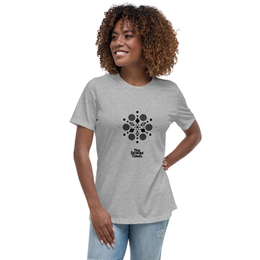 A person with curly hair smiles while wearing a light gray, comfortable women's tee featuring a black abstract dot pattern and the text "The Strange Times" written below the design. The person is also sporting light blue jeans against a black backdrop. She is wearing the WT002 ▪ T-Shirt by C3.